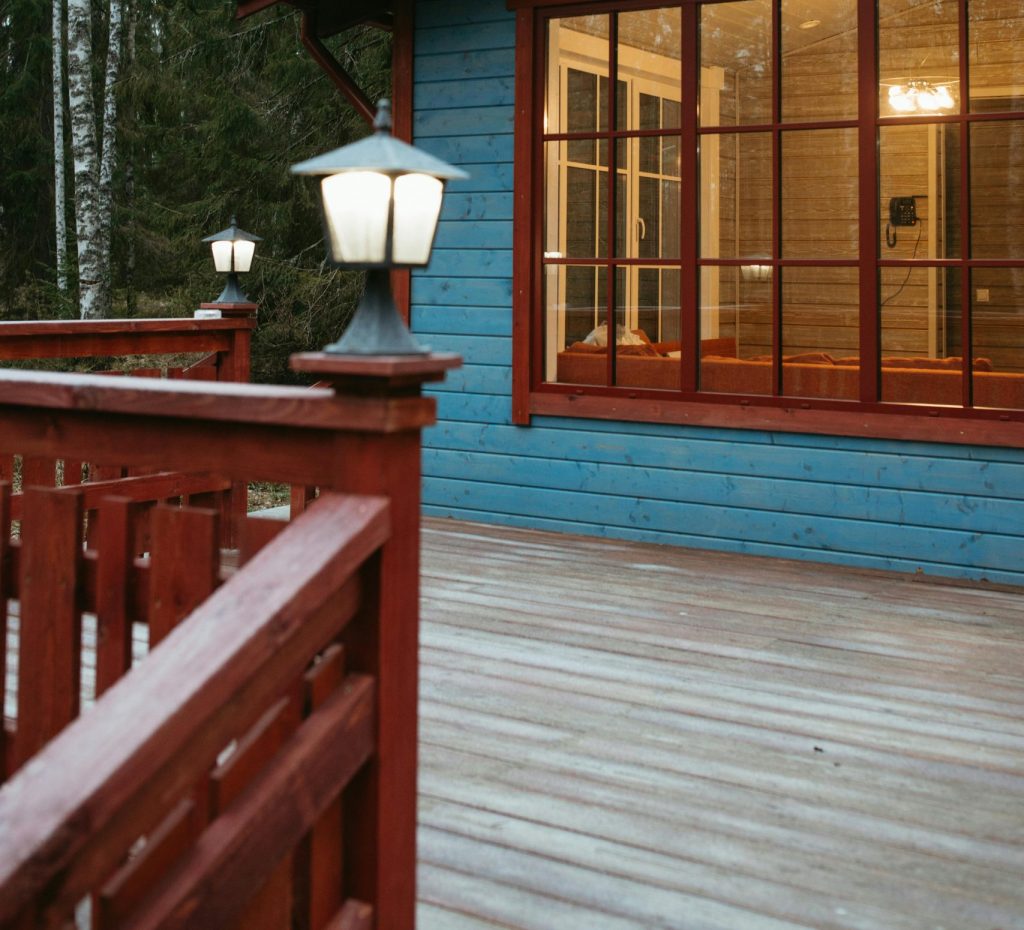 Warm view of a rustic wooden cabin surrounded by trees, featuring large glass windows and an inviting porch.
