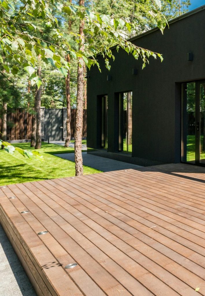 Stylish outdoor space with wooden deck and dining set, surrounded by lush greenery.