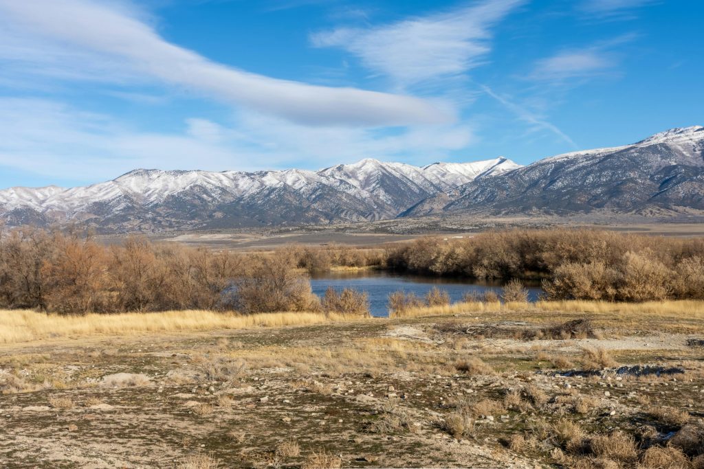 Picturesque scene of snow-capped mountains under a clear blue sky, reflected in a calm lake.