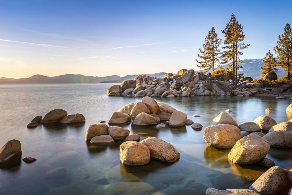 Tranquil sunset view over Lake Tahoe with rocks and pine trees near Glenbrook, NV