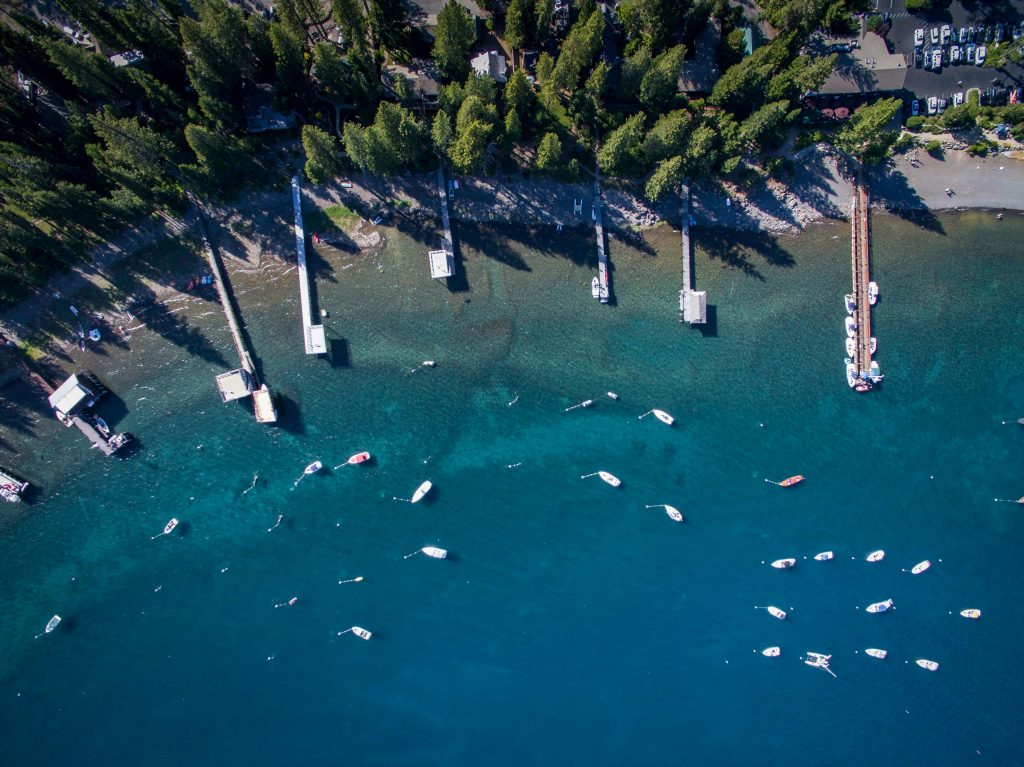A stunning aerial shot of boats by a pier on Lake Tahoe, surrounded by lush forests and clear blue water.